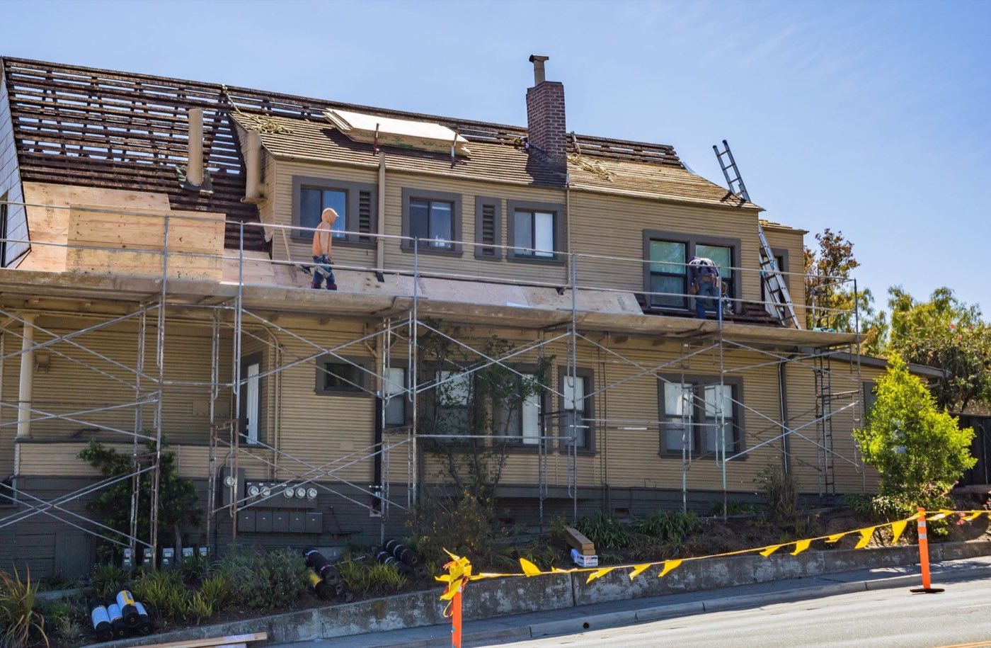 Contractors on scaffolding replacing the roof of a two-story family house on a sunny day.