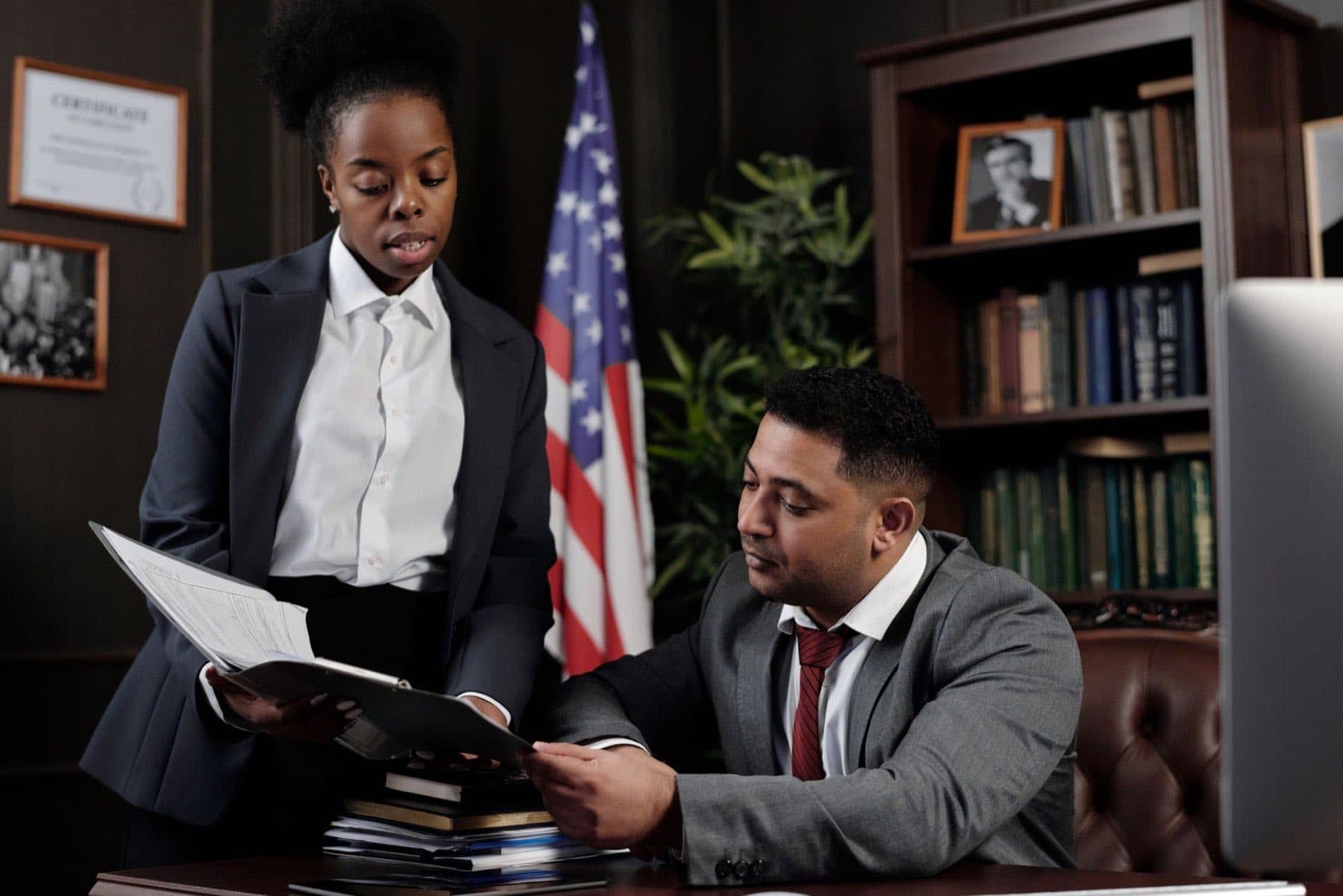 Two attorneys reviewing case documents together in a law office with bookshelves and an American flag.
