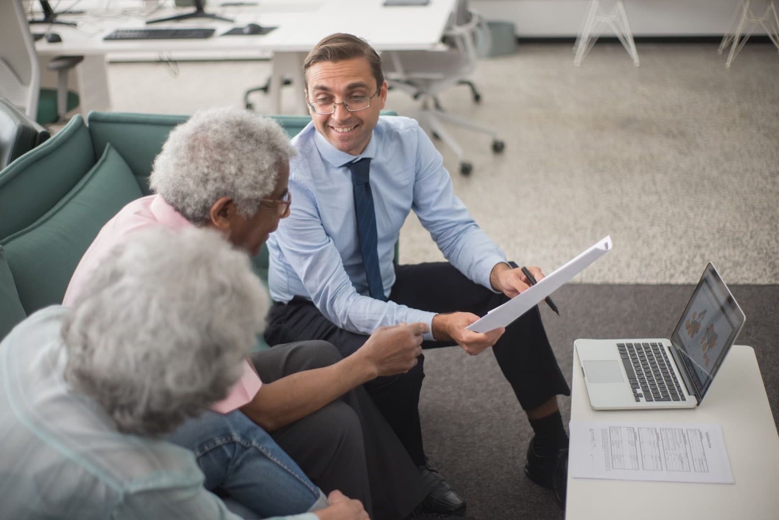 Financial advisor walking senior clients through a plan on paper in a modern office meeting.