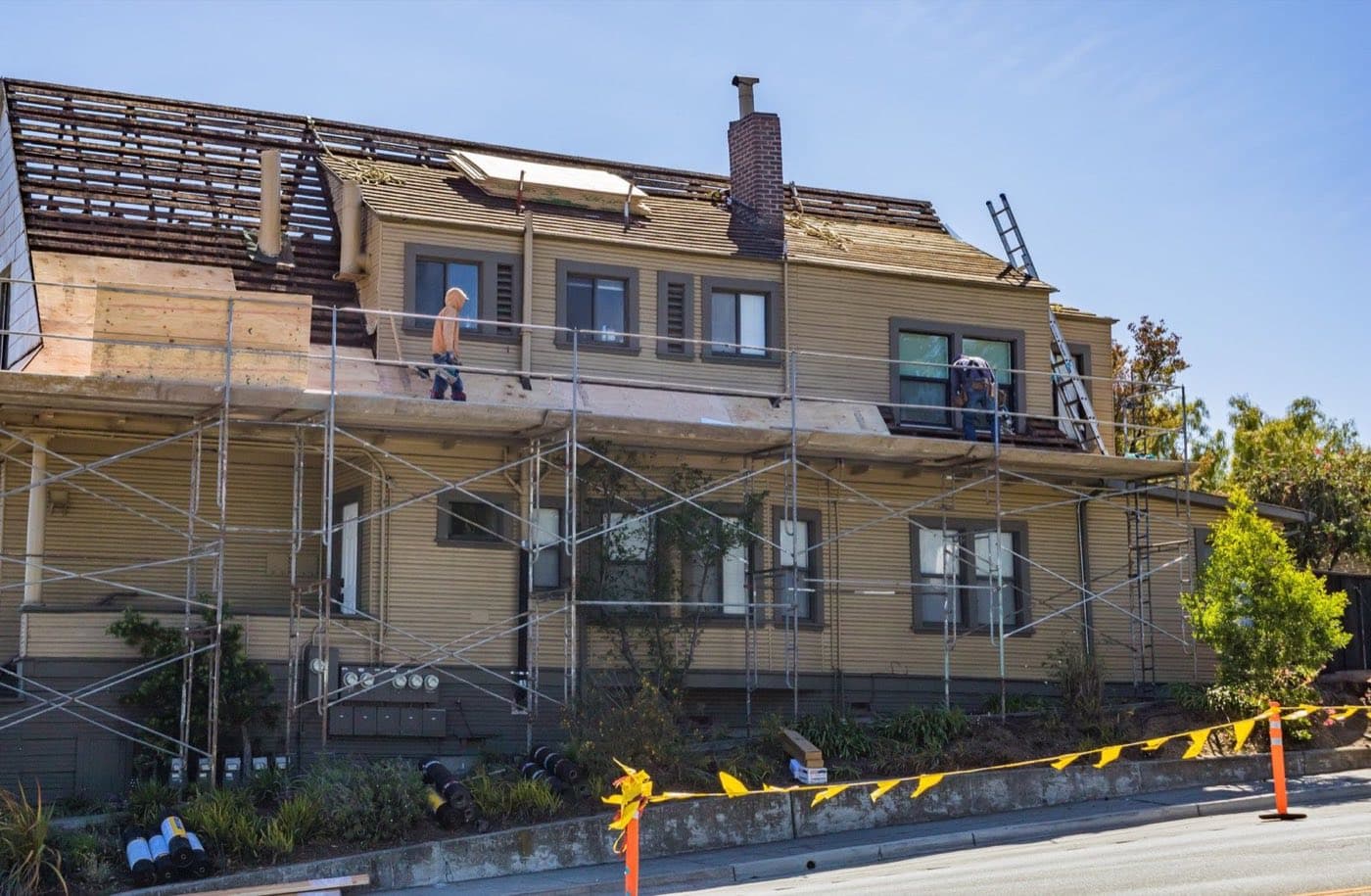 Contractors on scaffolding replacing the roof of a two-story family house on a sunny day.