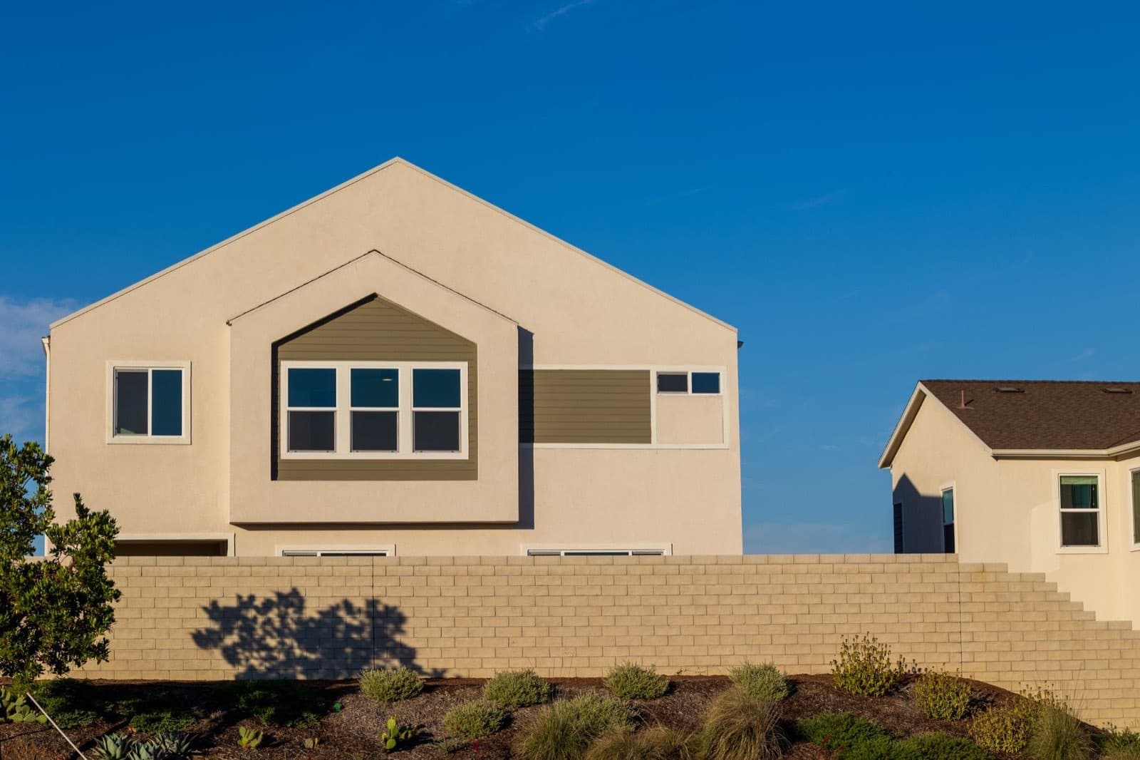 Sunlit facade of a modern two-story California suburban home under a clear blue sky.